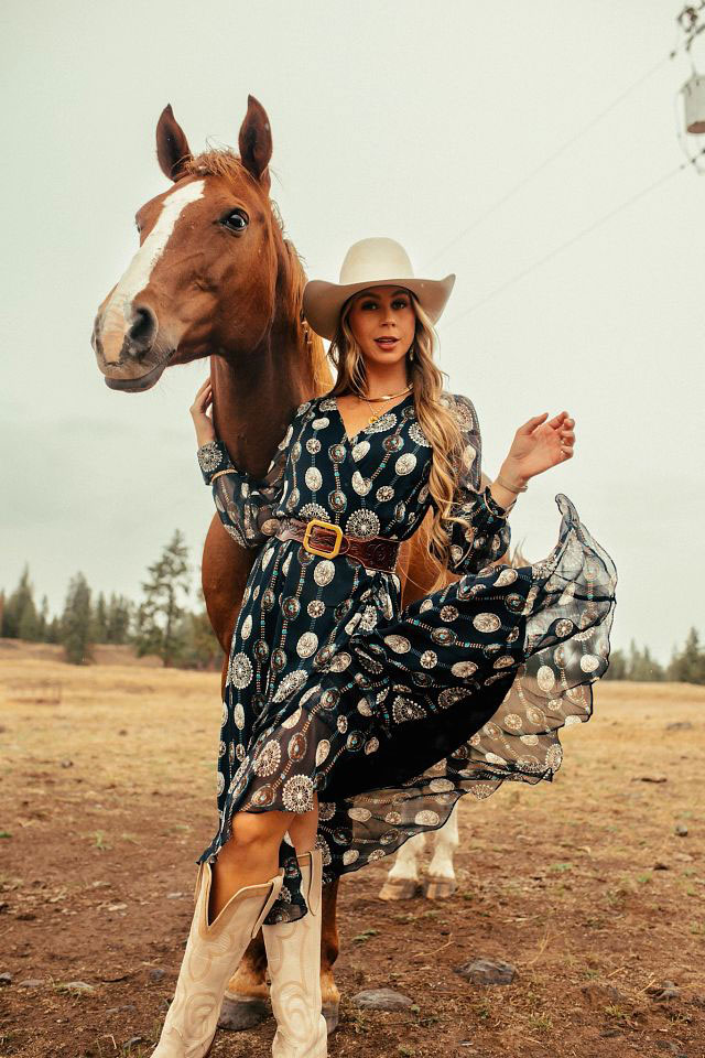 Una mujer con botas Justin parada delante de un caballo.